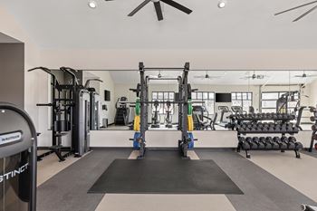 A gym with weights and dumbbells on the floor and a wall of windows